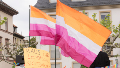 Symbolbild: Fahnen der lesbischen Sichtbarkeit und ein Demoplakat: Raus f&uuml;r lesbische Sichtbarkeit