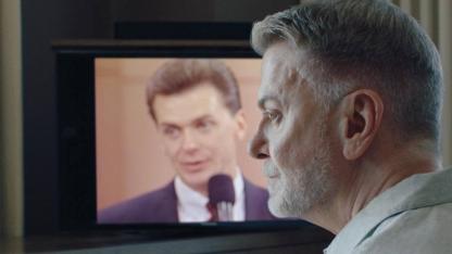 Mann im Profil vor einem Fernsehbildschirn, auf dem er in j&uuml;ngeren Jahren zu erkennen ist