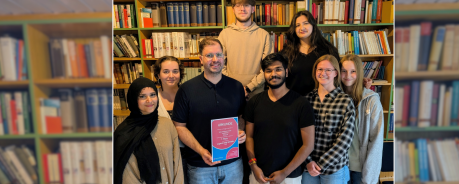 Patrick steht mit vielen jungen Menschen vor einem Bücherregal.