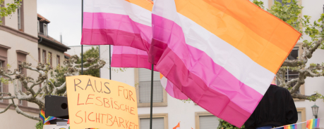 Symbolbild: Fahnen der lesbischen Sichtbarkeit und ein Demoplakat: Raus f&uuml;r lesbische Sichtbarkeit