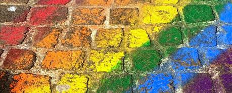Mit Kreide wurde eine Regenbogenflagge auf Kopfsteinpflaster gemalt. Die Regenbogenfahne ist das Zeichen für queere Menschen.
