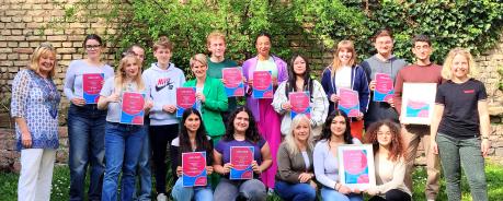 Gruppenfoto der Urkundenübergabe: Viele junge Menschen stehen zusammen und halten Urkunden hoch. Ganz links steht Elke Adler, ganz recht steht Mahela Stock.