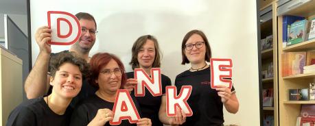 Gruppenbild: Mitarbeitende der AIDS-Hilfe. Jede Person trägt einen Buchstaben, die zusammen das Wort "Danke" ergeben.