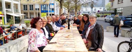 14 Personen sitzen um einen großen Tisch im Freien. Sie sind sehr gut gelaunt und warten auf ihr Essen.
