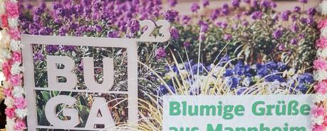 Poster der Bundesgartenschau in Mannheim. Sehr bunt mit vielen Pflanzen und Blüten. Davor der Schriftzug BUGA und Blumengrüße aus Mannheim. Unten das Logo der Deutschen Bahn