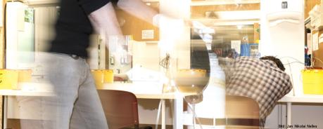 Safer Use: Was tun im Drogen-Notfall? Ein Drogengebraucher ist auf einem Tisch in sich zusammengesunken, im Vordergrund unscharf ein Mensch, der mit einem Sauerstoffbehälter zu Hilfe eilt