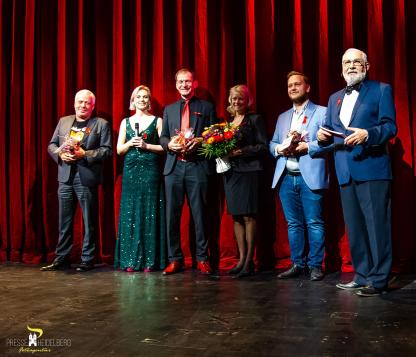 Gruppenfoto der Unterstützer*innen bei unserer Sternengala: Matthias Schiemer (Heidelberg Marketing), Lisa Koenen (Theater), Herr Kraus (Schirmherr) und seine Frau, Herr Müller (Weingut Adam Müller) und Wolfgang Erichson (Bürgermeister und Vorsitz Förderverein). Sie stehen auf der Bühne und haben Geschenke / Blumen in der Hand. Hinter ihnen ist ein roter Vorhang.