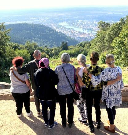 Gruppenfoto: 7 Menschen stehen auf einem Berg und schauen auf Heidelberg hinab. Sie umarmen sich und sind alle von hinten zu sehen.
