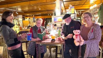 Gabriele Hönig und eine andere Person stehen an einem Tisch und lesen etwas vor. Links davon steht Jennifer Adler und hält eine Spendendose der Aidshilfe. Rechts davon steht Christine Klumb und hält einen Danke-Teddy.