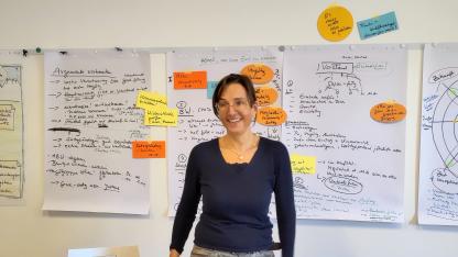 Christine Kirchner steht vor einer Wand mit beschriftetet Flipchart-Papieren