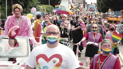 Titelbild der RNZ zum Dorfpride. Zu sehen ist ein Foto der Parade im letzten Jahr in Oftersheim. Im Vordergrund ist der Bürgermeister Jens Geiß, im Hintergrund sind ehrenamtliche Mitarbeiter*innen der AIDS-Hilfe Heidelberg.