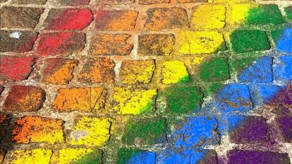 Mit Kreide wurde eine Regenbogenflagge auf Kopfsteinpflaster gemalt. Die Regenbogenfahne ist das Zeichen für queere Menschen.