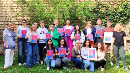 Gruppenfoto der Urkundenübergabe: Viele junge Menschen stehen zusammen und halten Urkunden hoch. Ganz links steht Elke Adler, ganz recht steht Mahela Stock.