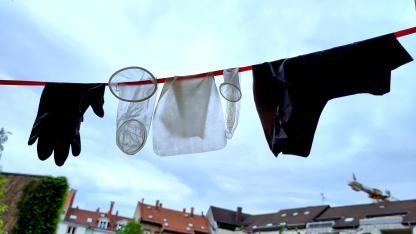 Auf einer Leine hängen ein Handschuh, ein Femidom, ein Kondom, ein Dental Dam und ein Loral-Höschen.